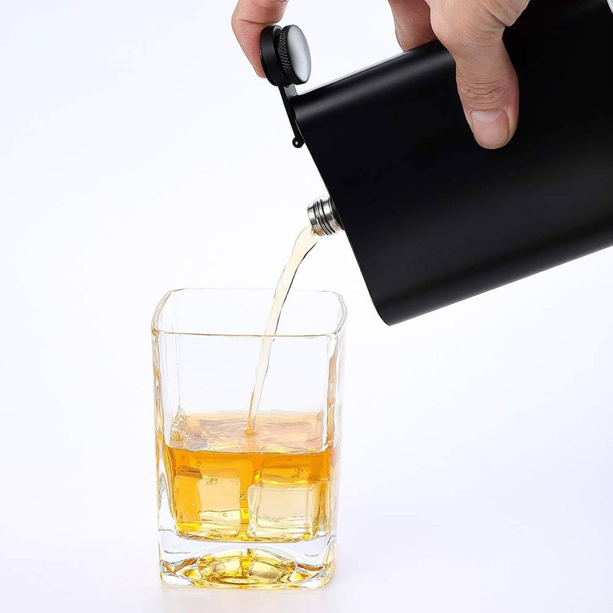 Black hip flask pouring golden liquid into a square tumbler