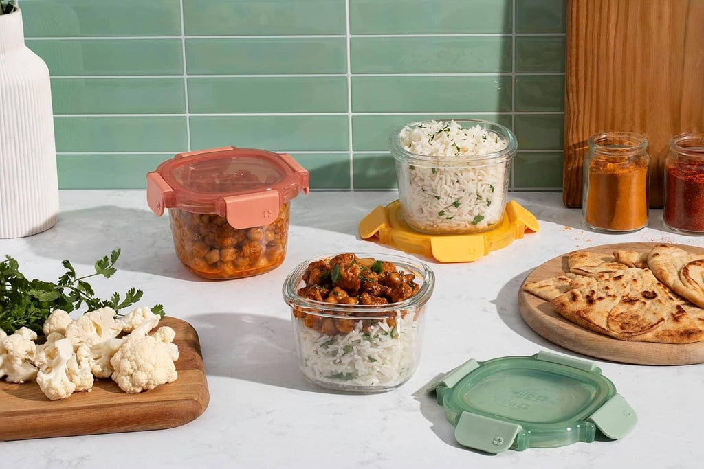 Glass meal prep containers with colored lids on kitchen counter, with food inside