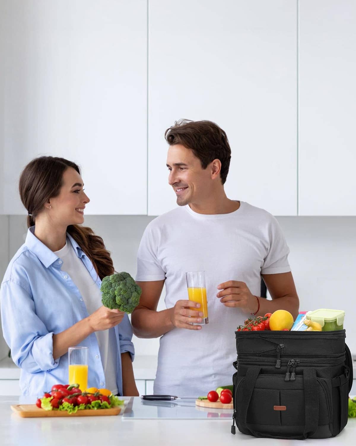 Black double-decker insulated lunch box with handle, worn on a table for meals.
