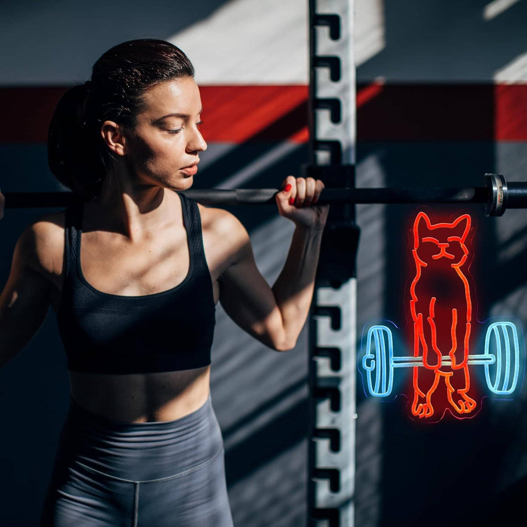 Neon cat lifting weights sign glowing red-orange cat with blue dumbbells beside exercise equipment