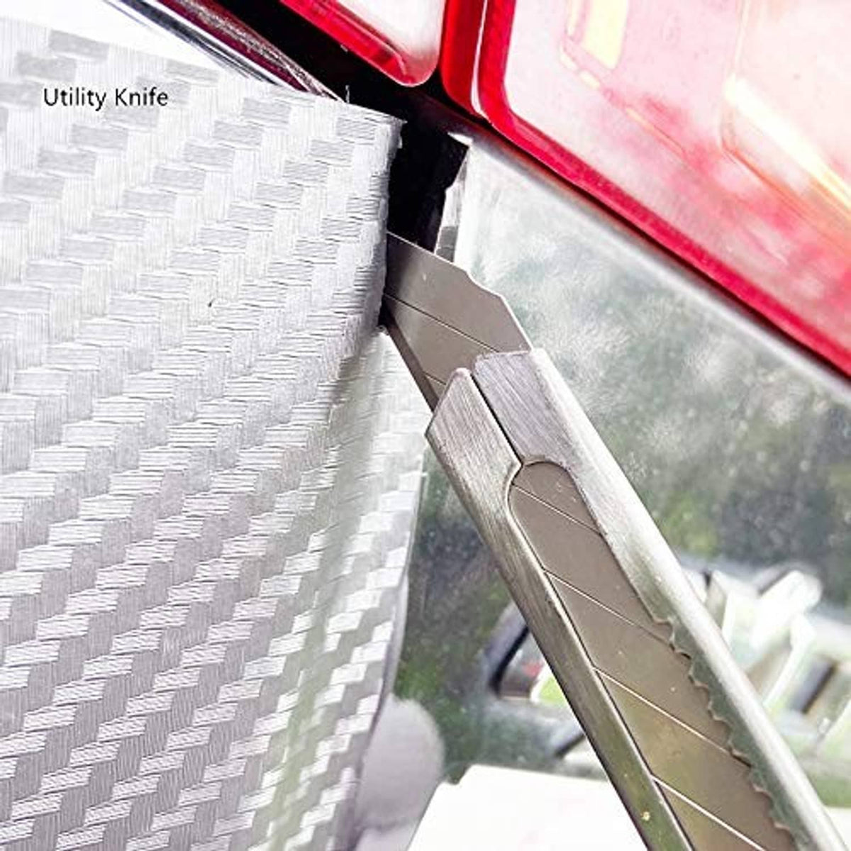 Utility knife cutting carbon-fiber window tint film along a sharp edge
