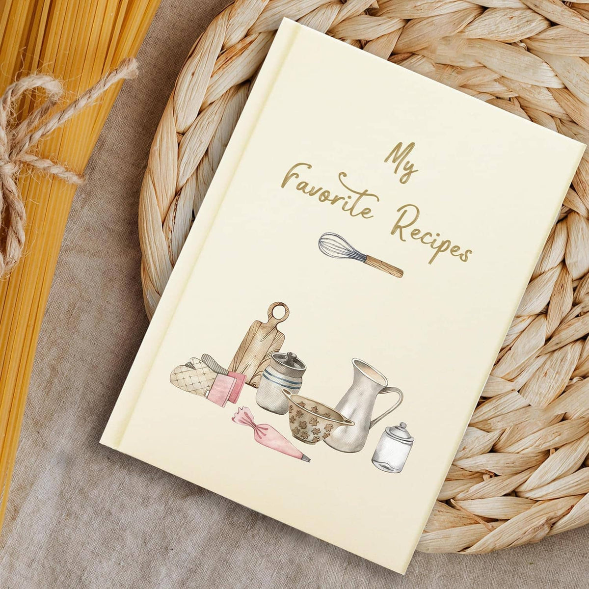 Cream hardcover recipe book lying on woven mat, “My Favorite Recipes” cover illustration
