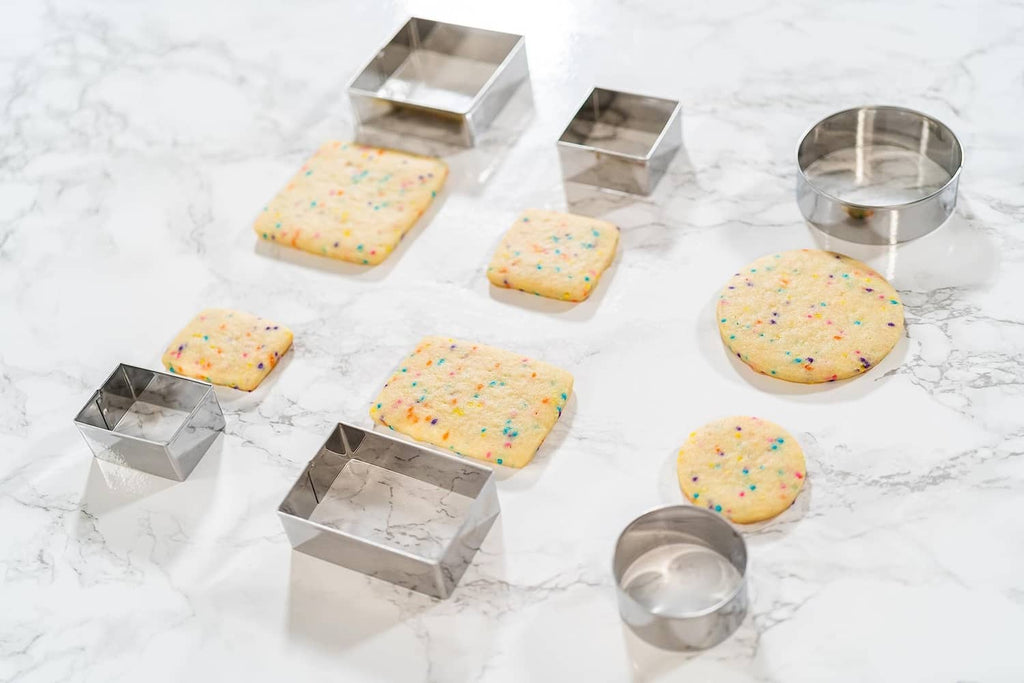 Stainless steel round cookie cutters with baked sprinkle cookies and empty rings.