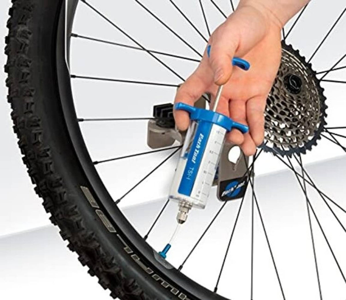 Hand using blue tubeless sealant injector at bicycle wheel valve