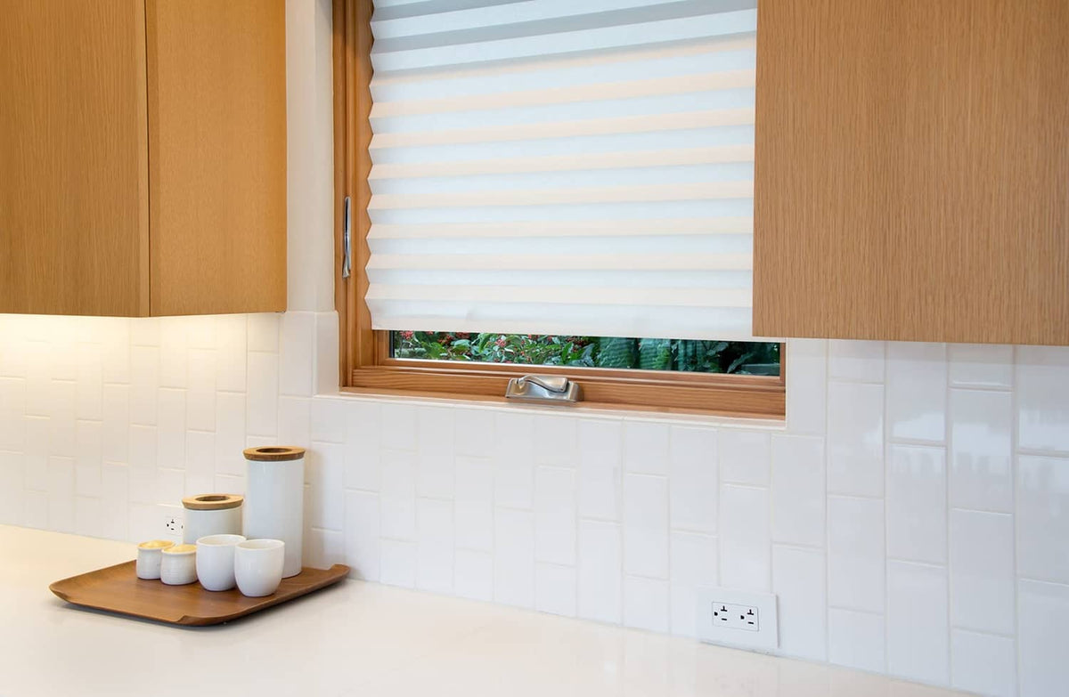 White pleated paper window shade partially lowered above a kitchen backsplash