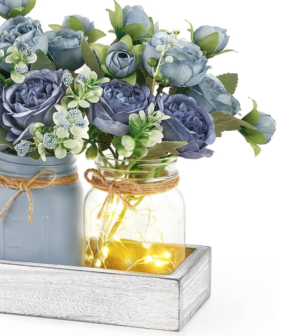 Close-up of blue faux roses and greenery in grey-blue mason jars with warm LED lights