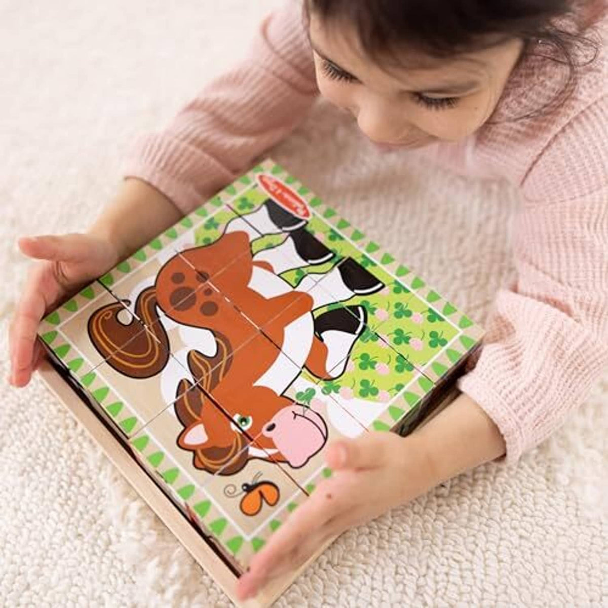 Child assembling a farm cube puzzle in a wooden tray with cow and dog pieces