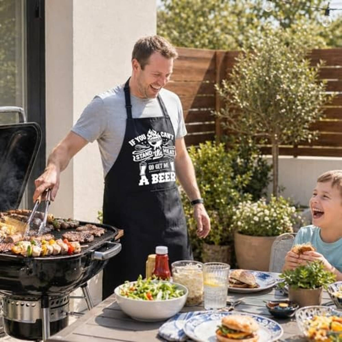 Black waterproof BBQ apron on man at grill; beer graphic and dual front pockets.