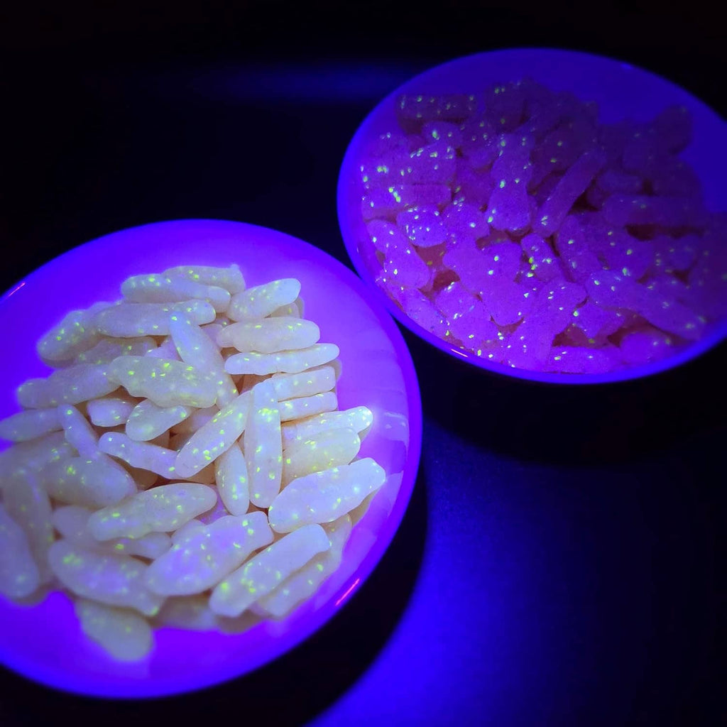 Neon-glowing gummy candy pieces in bowls under blacklight, confetti visible
