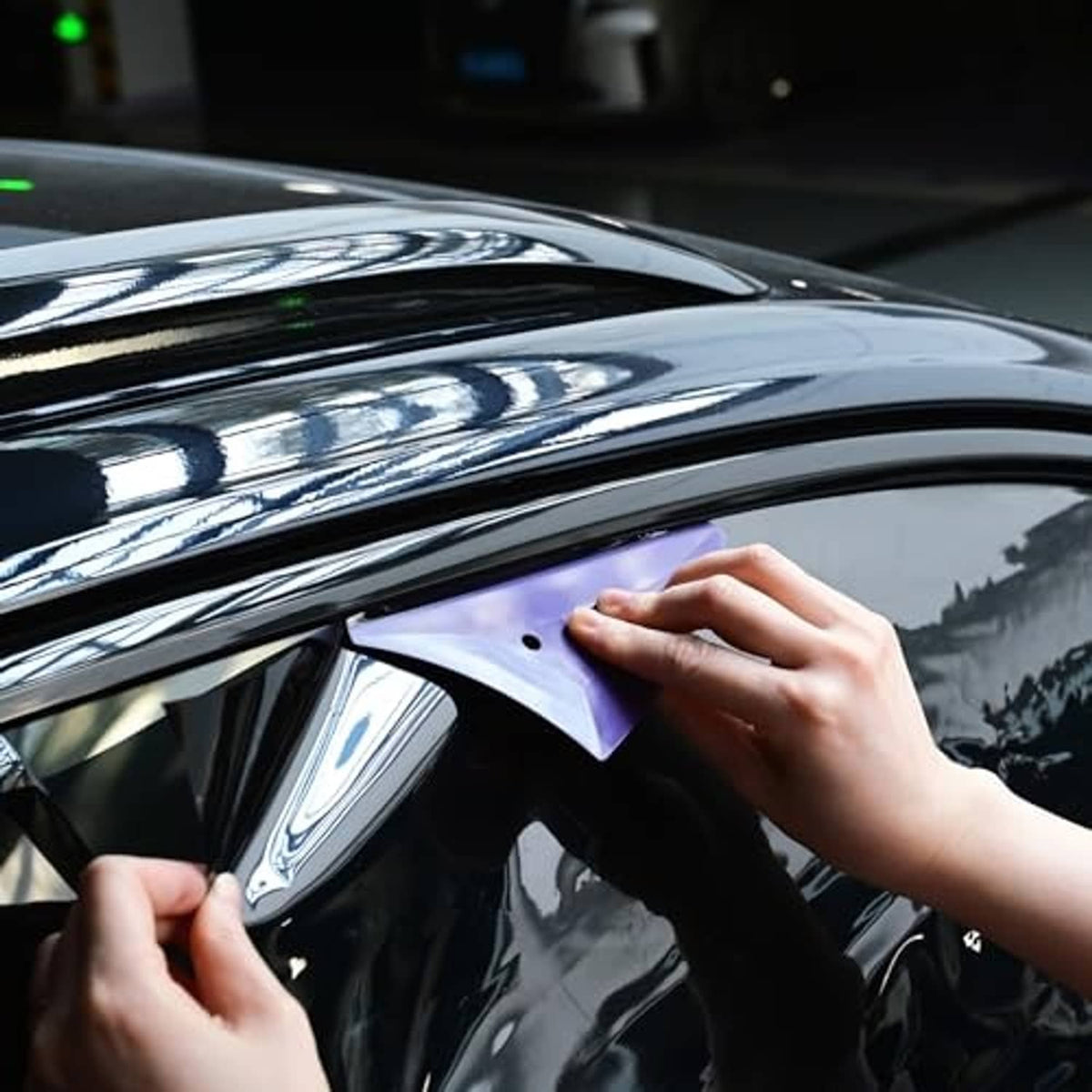 Hands smoothing window tint film with purple triangle squeegee on car glass