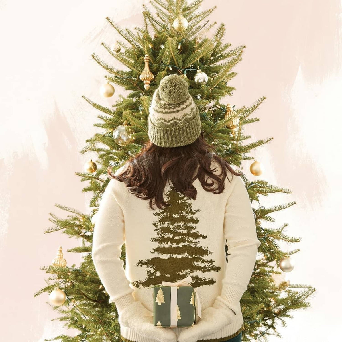 Person holding a wrapped gift in front of a decorated Christmas tree