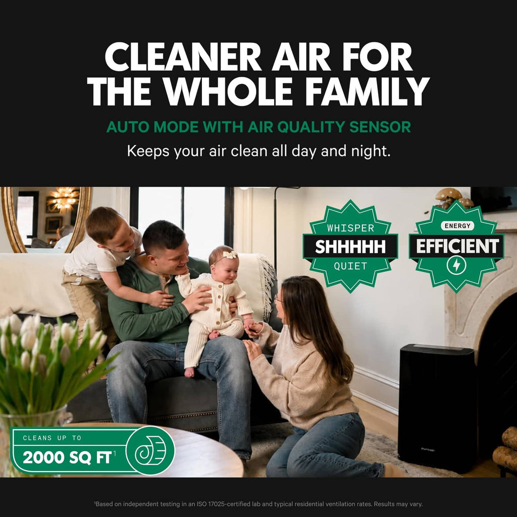 Black air purifier on the floor beside sofa, with indicator lights on the front.