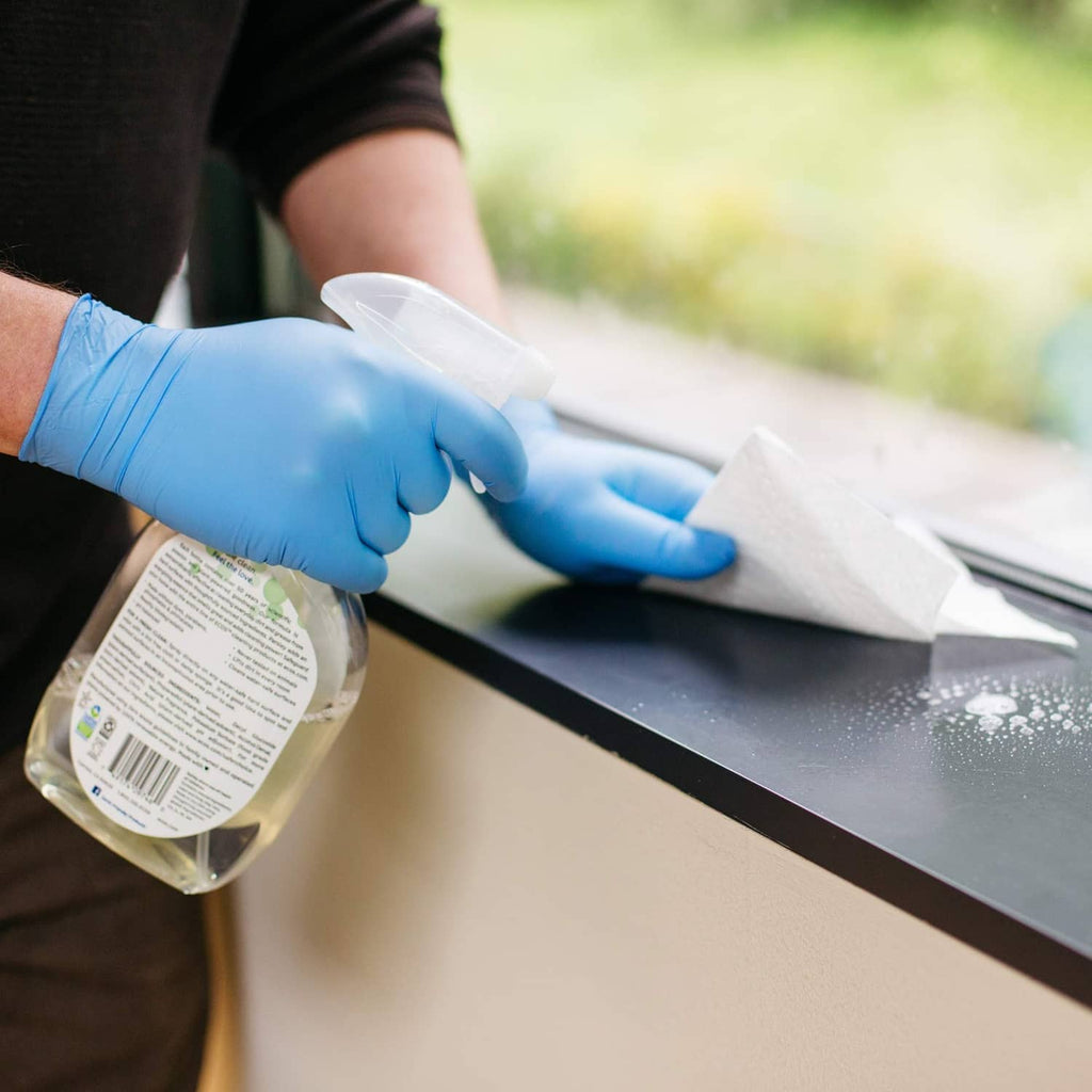Blue nitrile glove hand spraying cleaner on a countertop