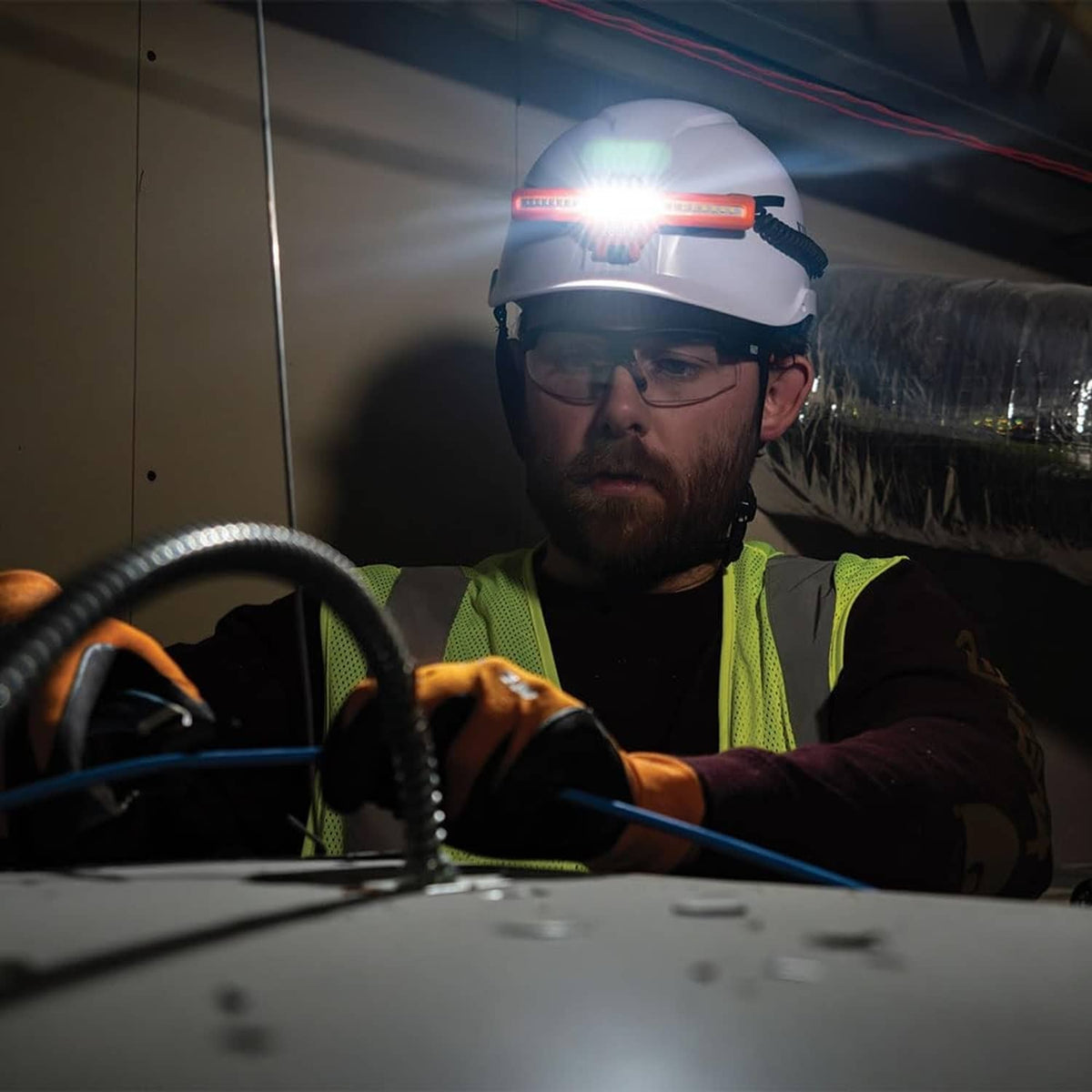 Worker wearing orange rechargeable LED headlamp with bright light above