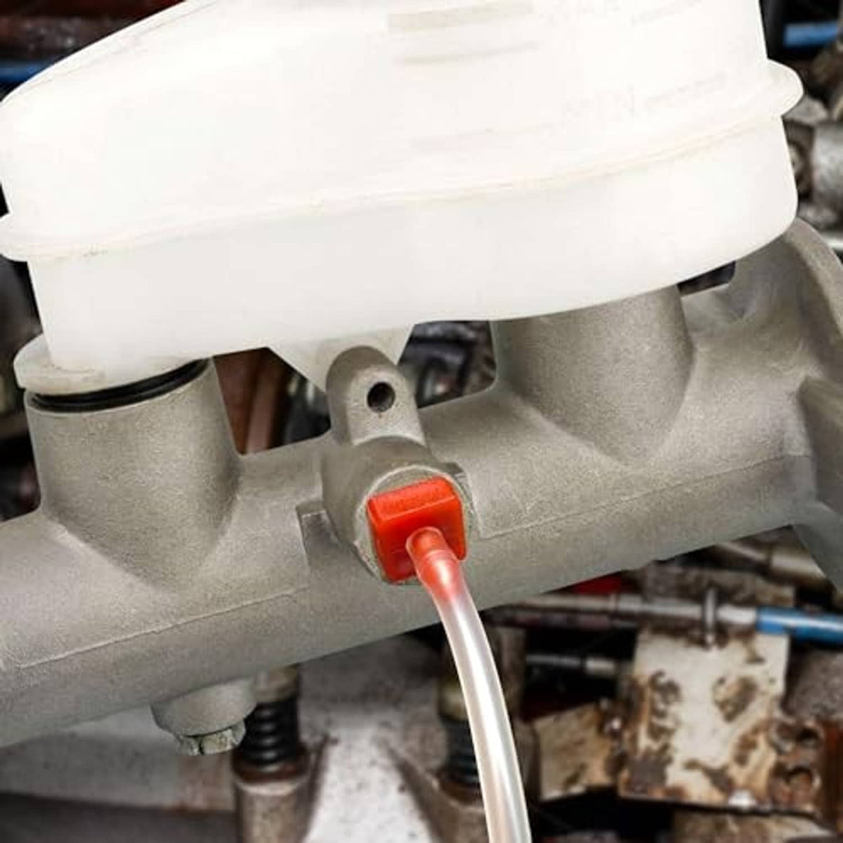 Close-up: brake master cylinder outlet with clear hose and red push-in bleeder fitting