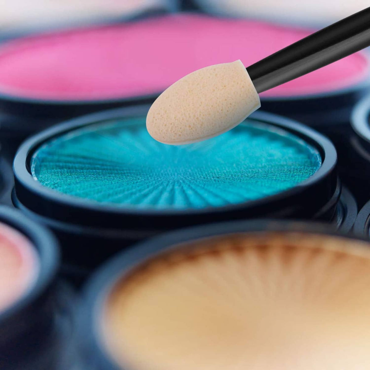 Close-up sponge tip makeup brush dipping into turquoise eyeshadow in a compact