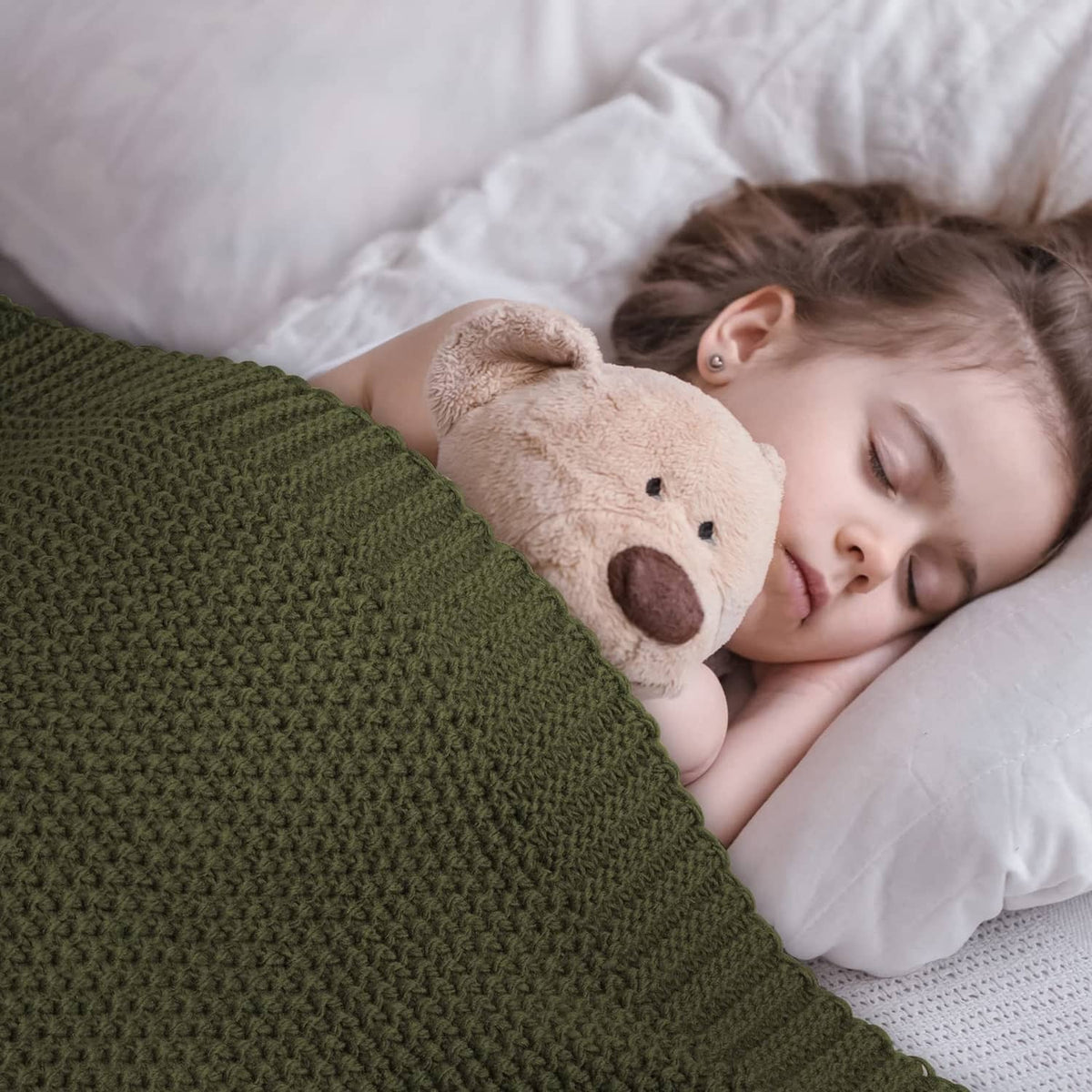 Olive green knit throw blanket with child cuddling a plush teddy bear.