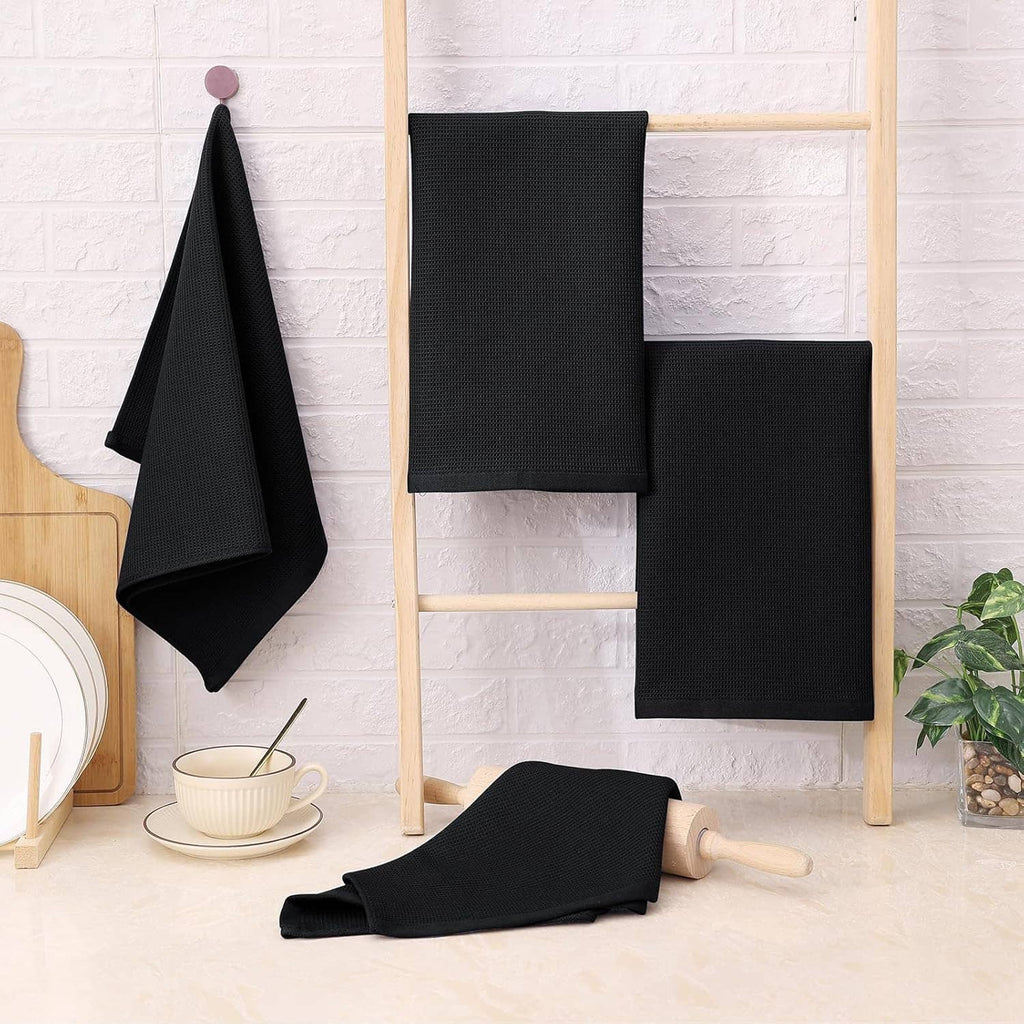 Black waffle weave cotton kitchen towels on a wooden rack, folded and hanging