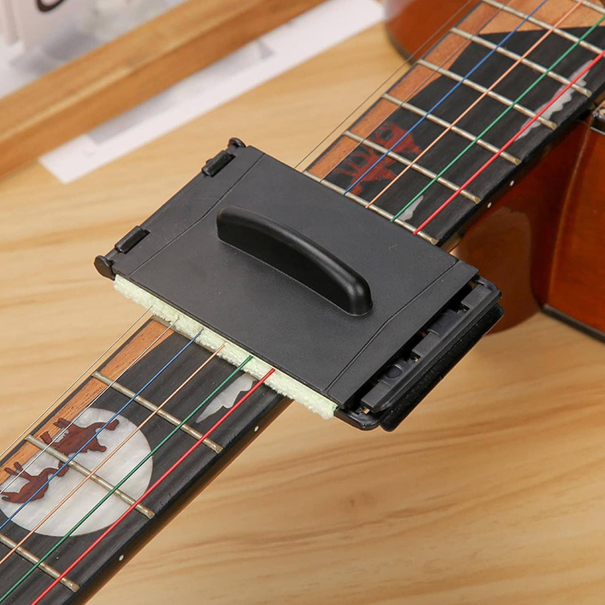 Guitar string cleaner tool placed on guitar strings with cloth pad in black case
