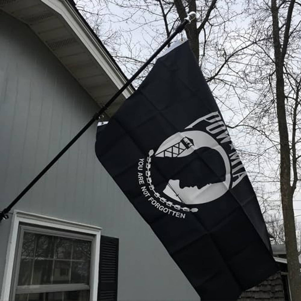 Black POW*MIA outdoor flag with white emblem and text, flying on pole outdoors