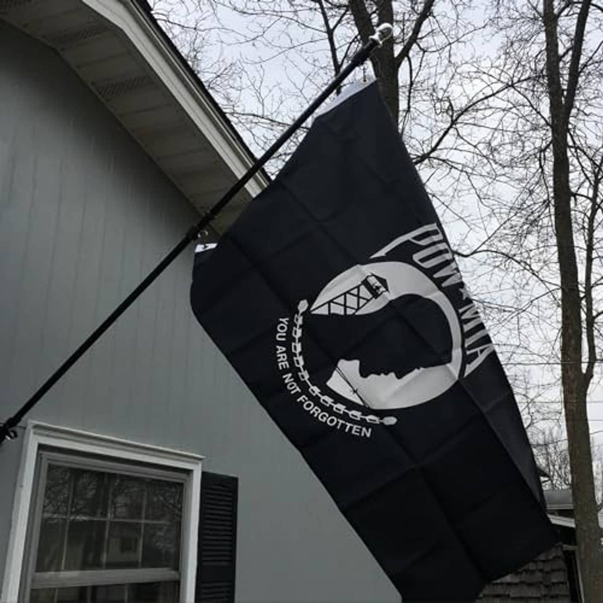 Black POW*MIA outdoor flag with white emblem and text, flying on pole outdoors