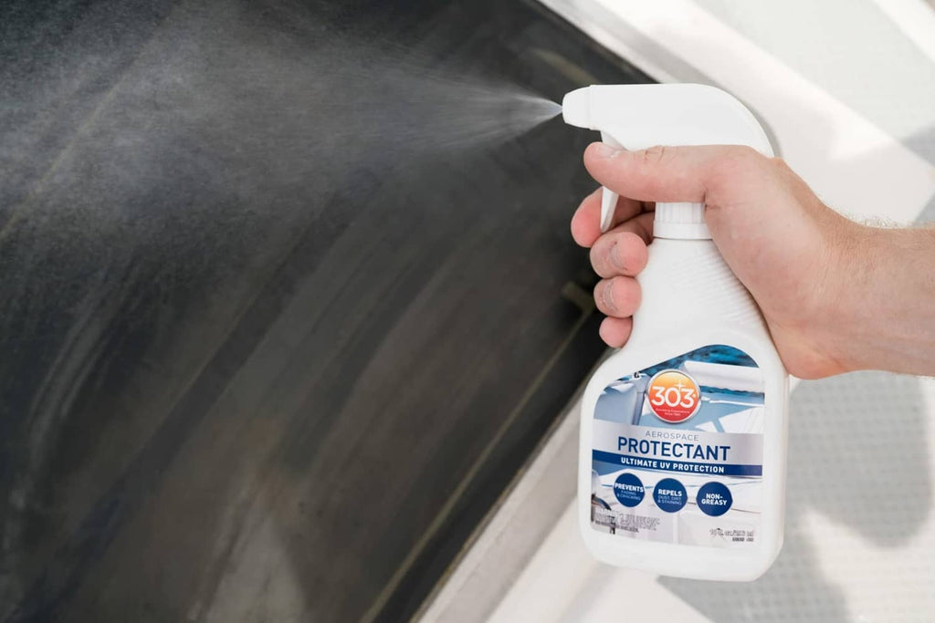 Hand using white trigger sprayer to apply protectant to dark vehicle trim