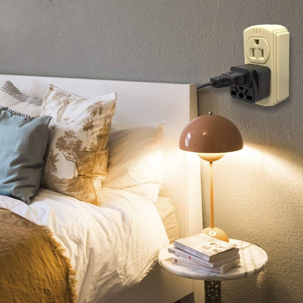 Black travel plug adapter plugged into a wall outlet next to a bedside lamp