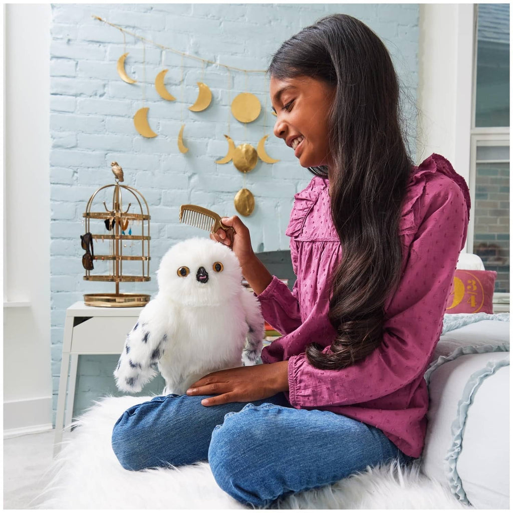 White interactive owl plush with a person holding a gold comb accessory beside it.