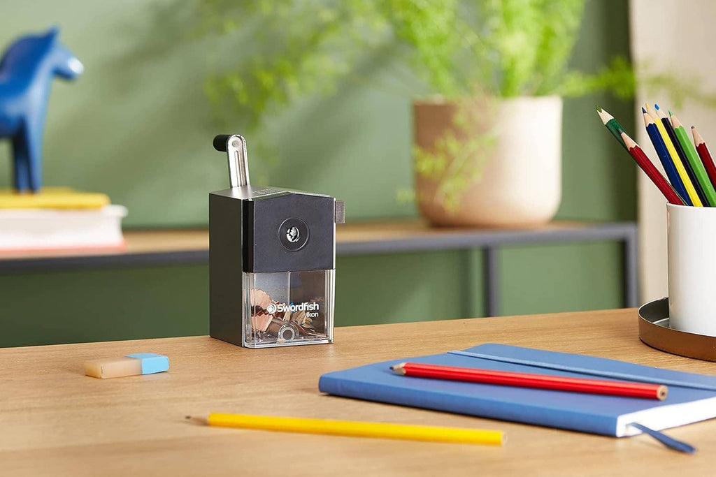 Small black pencil sharpener on desk with clear shavings bin and side handle