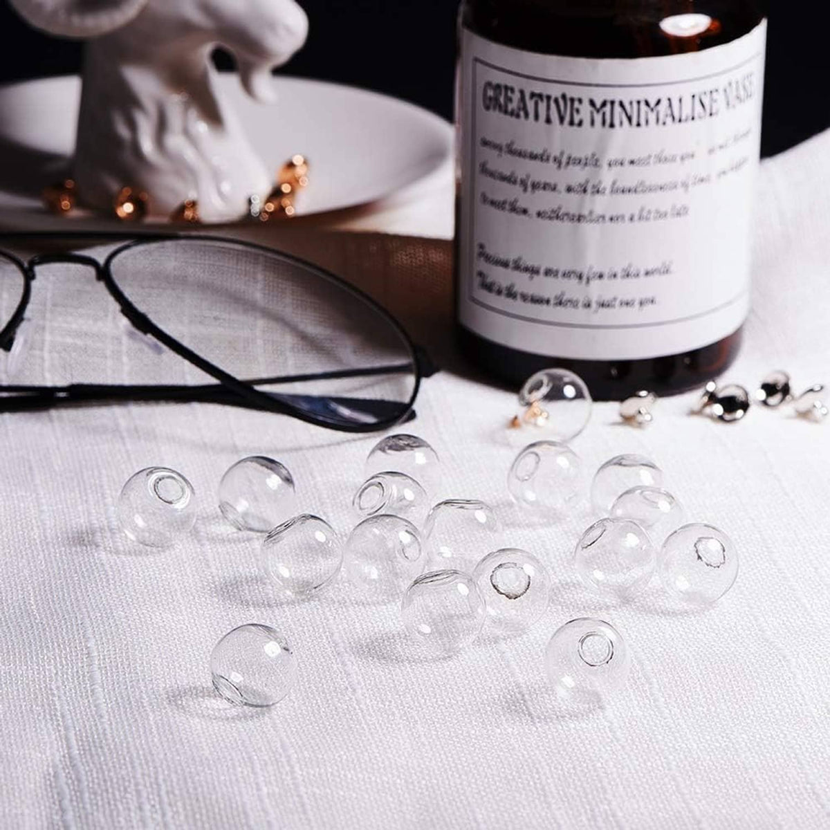 Clear mini glass globe bottles scattered on fabric with a bottle of jewelry filler nearby