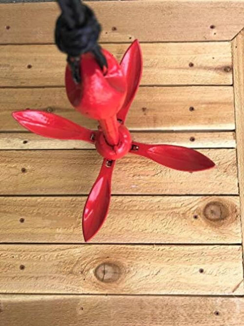 Red grapnel anchor with four flukes on a length of black rope
