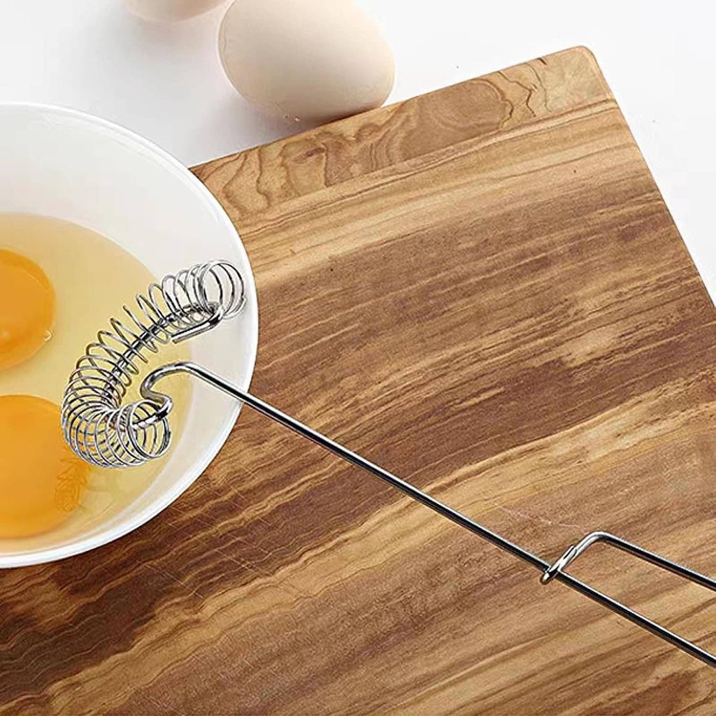 Stainless steel coil whisk resting in a bowl with flat handle on wooden surface