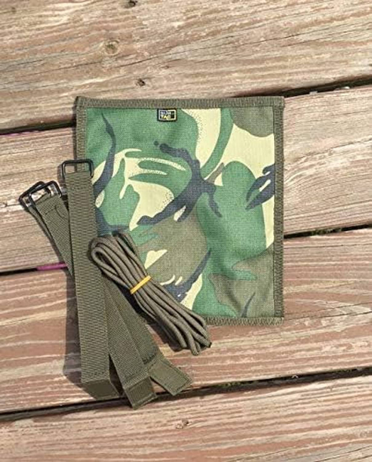 Multicam patch suppressor cover with tan webbing straps and bundled cord on wooden surface