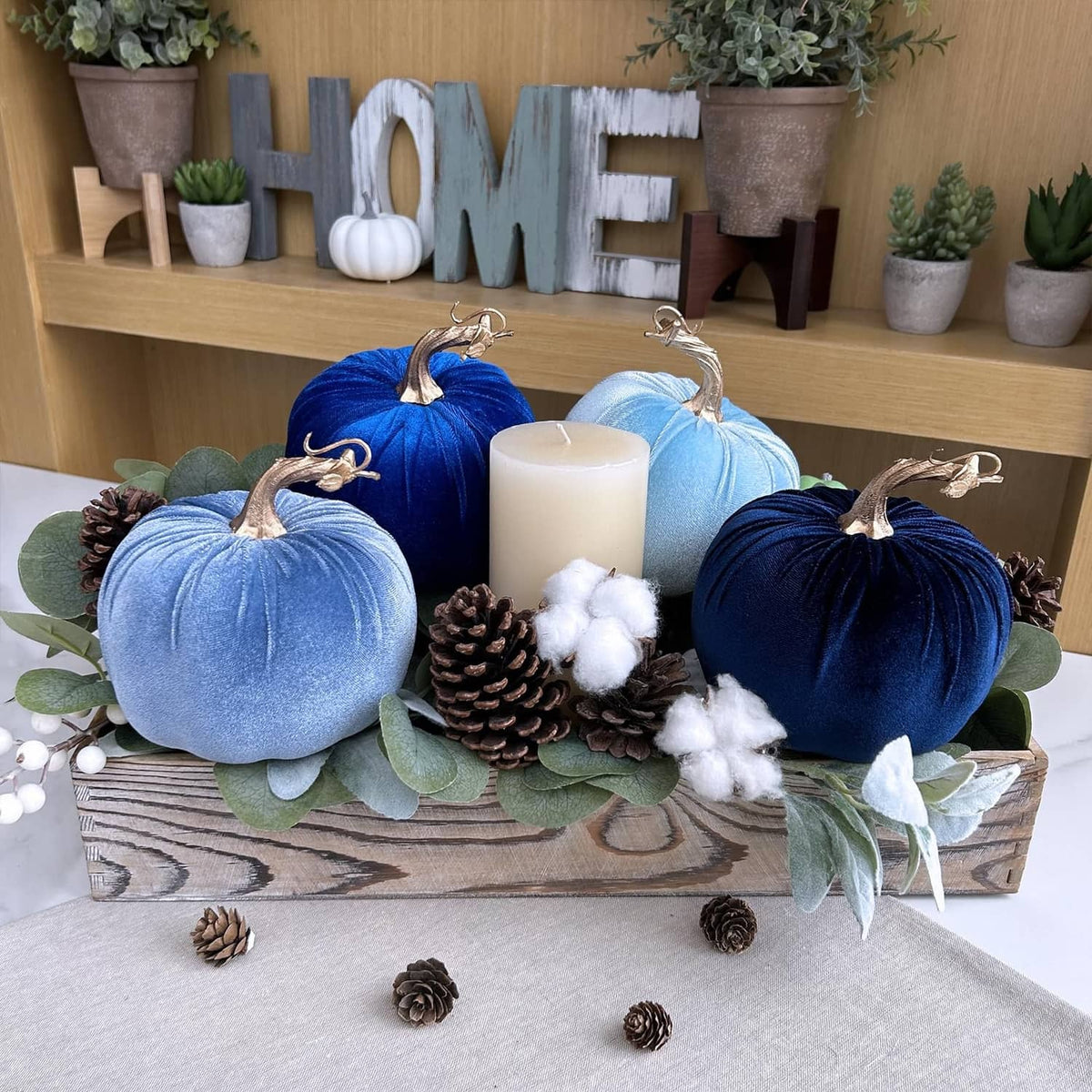 Four blue faux velvet pumpkins with gold stems and loops, arranged around cream candles