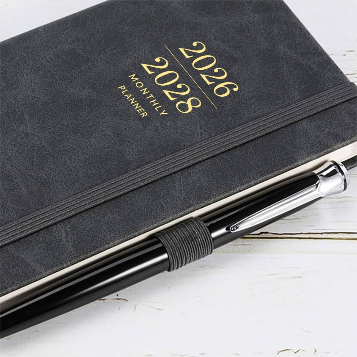 Dark faux-leather pocket planner cover with gold “2026–2028” text and pen on desk