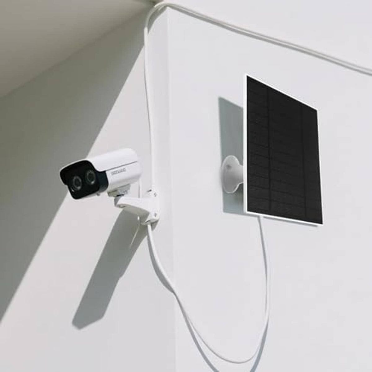 Black flexible solar panel connected to security camera on exterior wall with cords