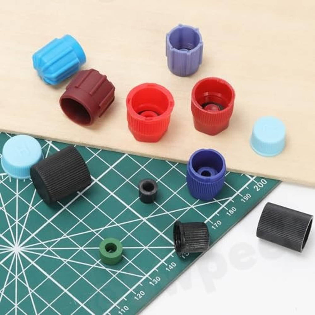 Assorted A/C valve core caps in black, red, blue, purple, and green on work surface