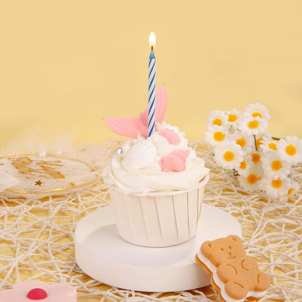 Single lit striped birthday candle with pink and blue stripes on frosted cake