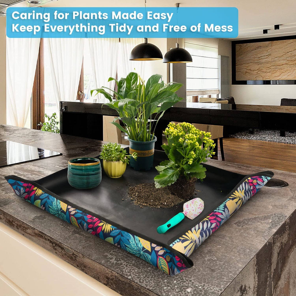 Black plant repotting tray with colorful leaf print border and gardening tools on top