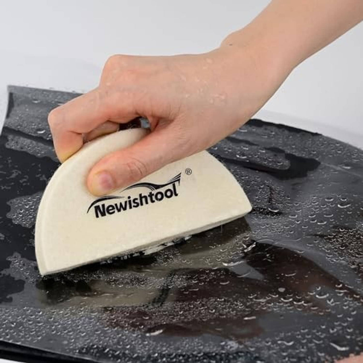 Beige wool felt squeegee pad smoothing dark surface, hands hold the tool
