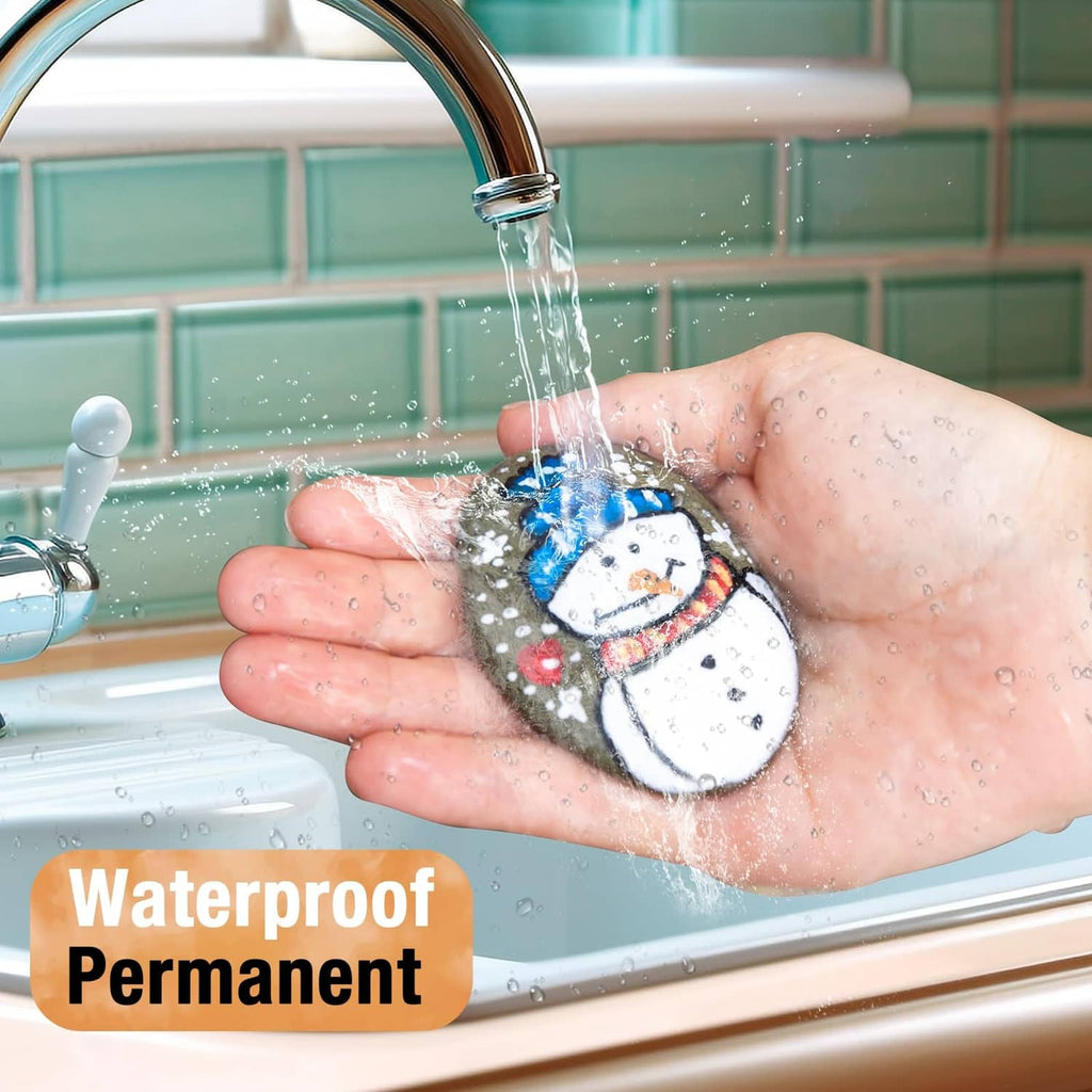 Hand holding a white waterproof paint marker dispensing ink onto a snowman drawing
