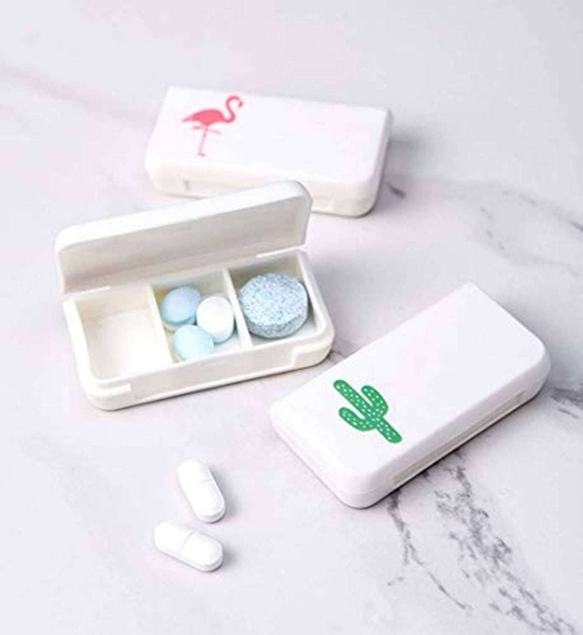 Four small white pill organizers with cactus/flamingo icons, open tray with tablets inside