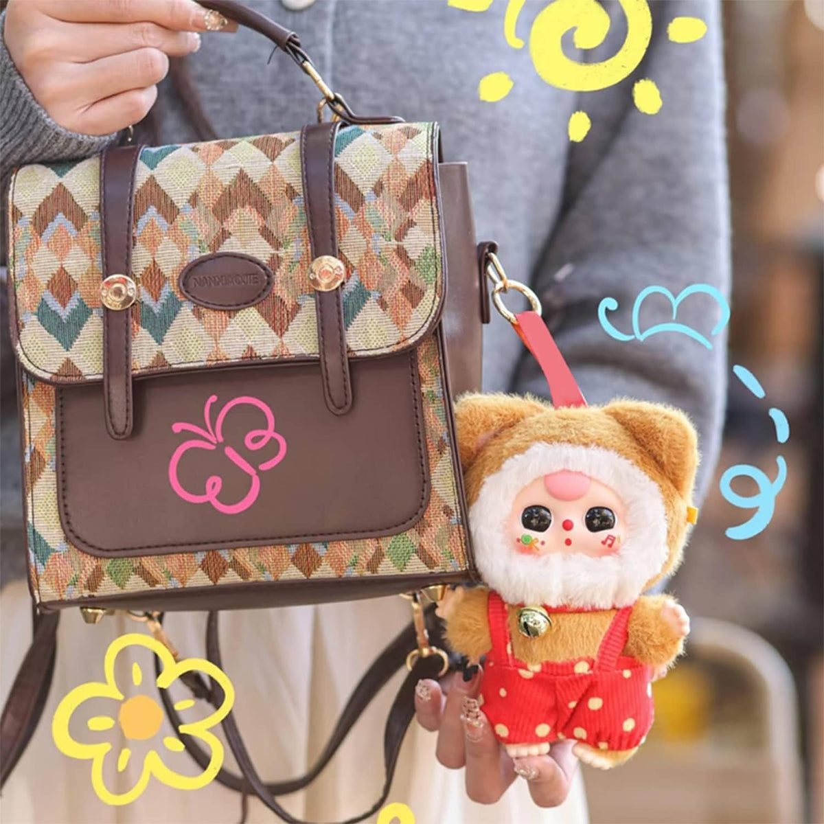 Small plush cat doll in a brown hat and orange overalls, with gold bell charm.