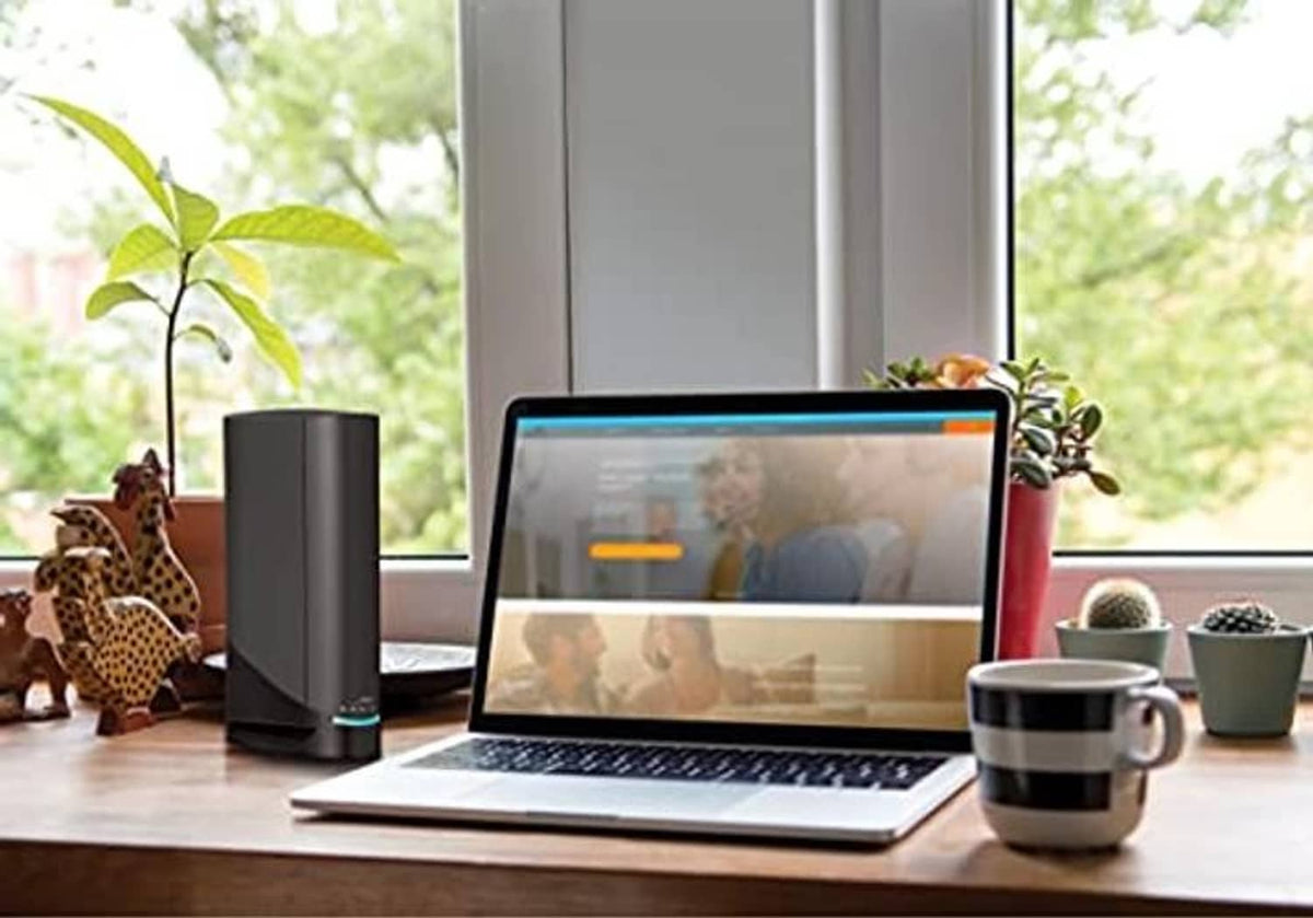 Black modem tower on desk next to laptop and coffee mug