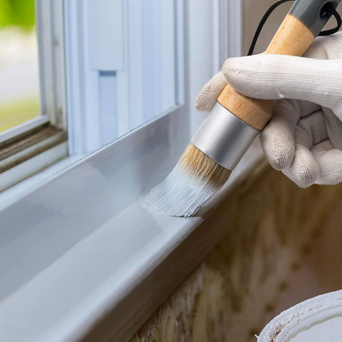 Small wax paint brush spreading white wax on window sill, light wood handle