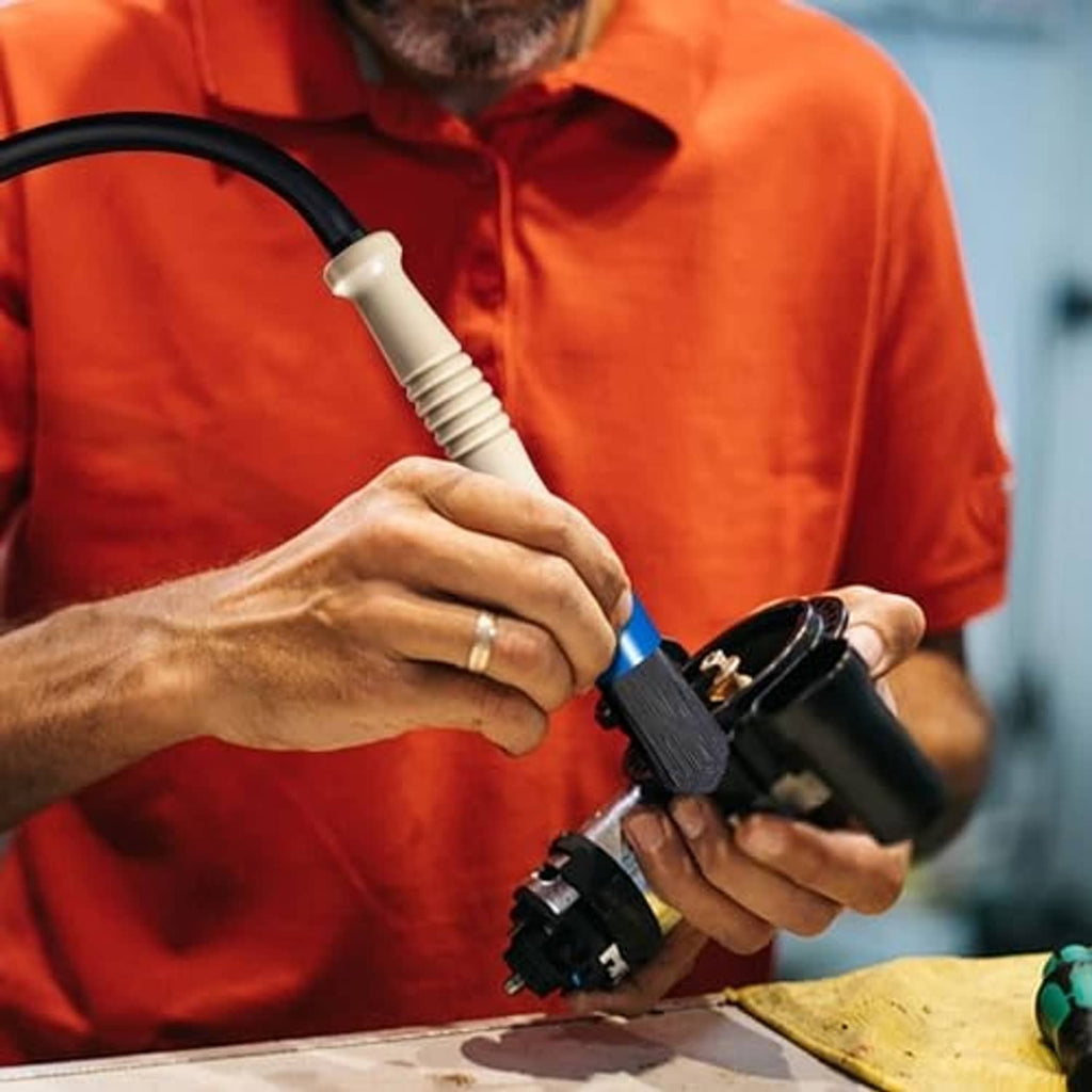 Parts cleaning brush with blue handle and black hose held for washing components