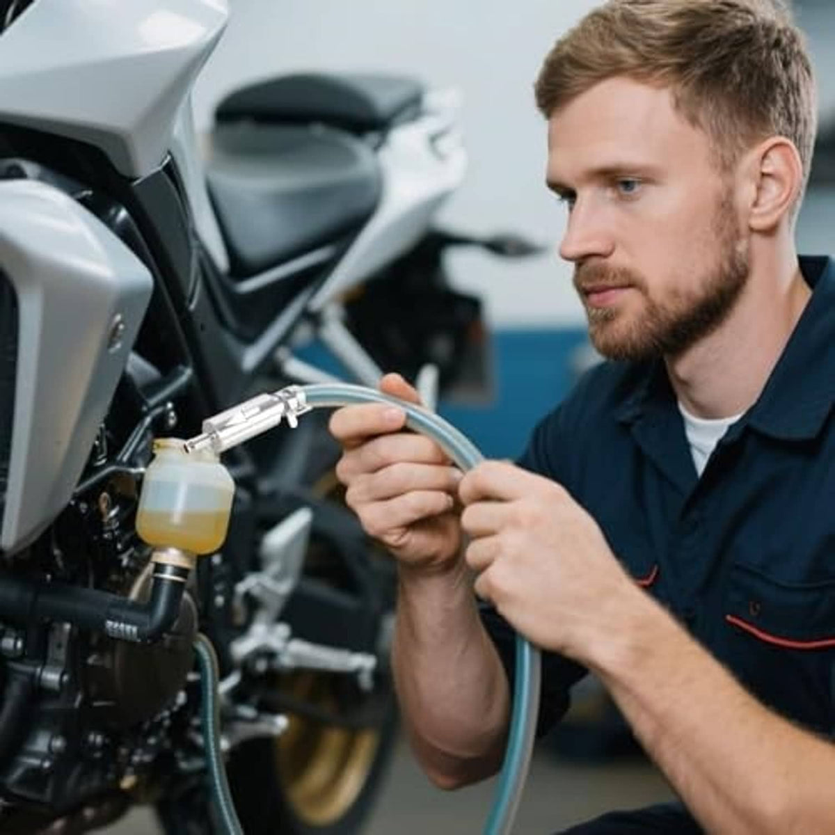 Motorcycle mechanic using brake bleeder kit with clear hose and valve tool