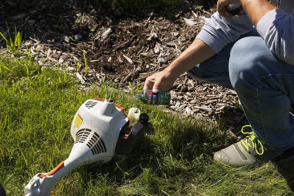 Small engine treatment bottle being poured near a lawn mower