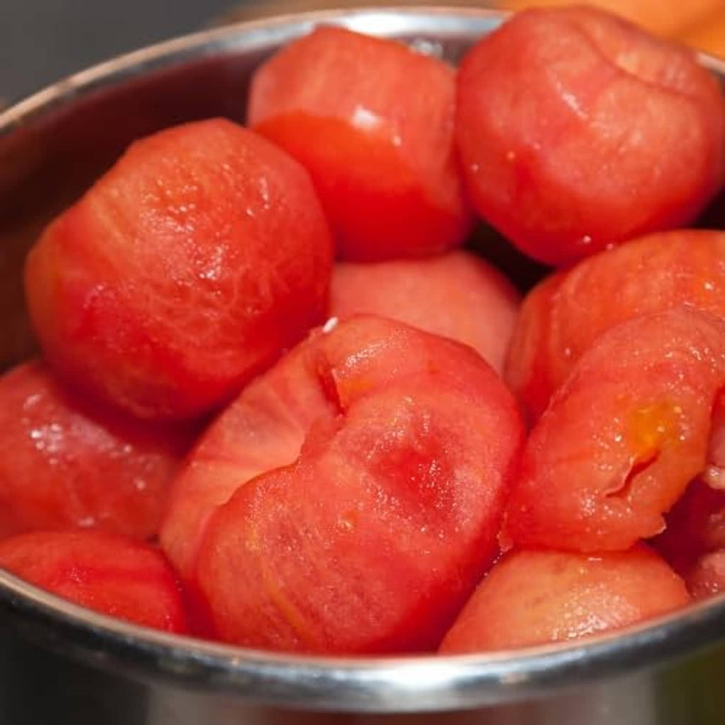 Pealed tomatoes in metal bowl, glossy red pieces