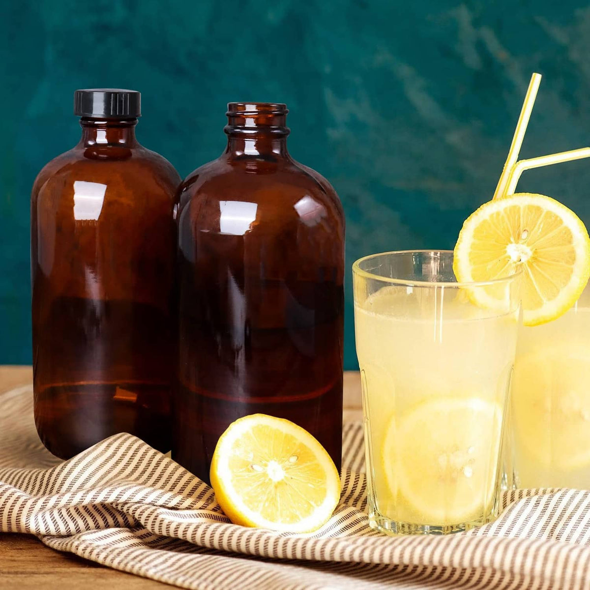 Two amber glass bottles with black caps beside cut lemons and a glass drink.
